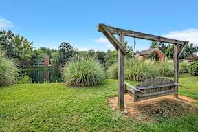 a swing bench on the grass next to a pond