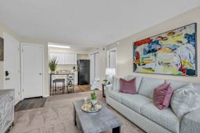 A living room with a grey couch and a painting on the wall.