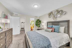 A bedroom with a bed, dresser, and a plant.