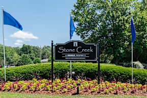 the sign for stone creek park in front of a garden with three flags
