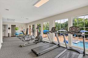 a gym with cardio machines and windows with a pool