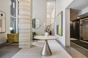 A white marble column stands in a room with a round table and a mirror.