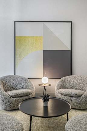 A modern living room with a grey sofa, a round table and a framed artwork on the wall.