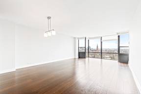 A room with a wooden floor and a large window overlooking a cityscape.