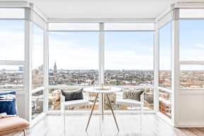 A white room with a table and chairs in front of a window overlooking a cityscape.