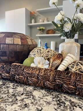 A wicker basket filled with various objects including a white vase with flowers, a brown egg, and a green fruit.