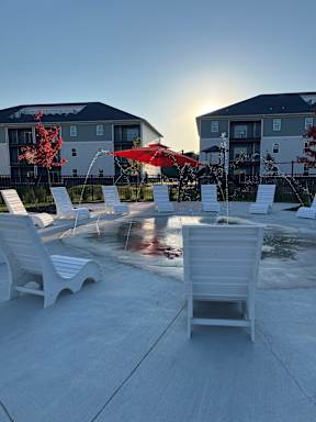 A sunny day at a poolside with white chairs and a red umbrella.