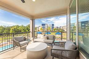 A balcony with a white couch, grey armchair, and a white ottoman at The Preserve at Preston Trails Apartments, Cedar Hill, TX, 75104