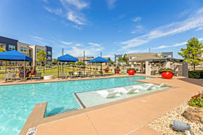 A swimming pool with a glass divider in the middle and a blue umbrella on the left at The Preserve at Preston Trails Apartments, Cedar Hill, Texas