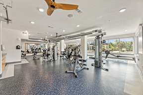 A spacious gym with a variety of equipment and a ceiling fan at The Preserve at Preston Trails Apartments, Texas, 75104
