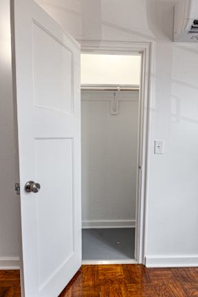 A white door with a silver handle is open to a small, empty room with a white wall and a wooden floor.