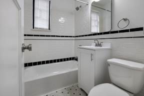 A white bathroom with a black and white tile border, with sink, toilet and bathtub included,  at Marleigh apartments located in Indianapolis, IN
