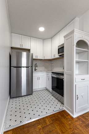 A kitchen with a refrigerator, cabinets, and a tiled floor.