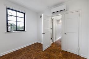 A room with a window, wooden floor, and two white doors.