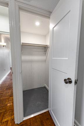 A white door with a silver handle is open to a small room with a wooden floor.