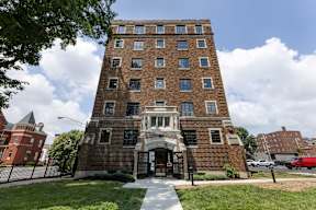 A tall brick apartment building with a white entrance and a fence in front  at Marleigh apartments located in Indianapolis, IN