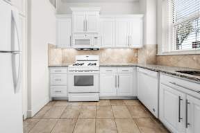 A white kitchen with a fridge on the left and a stove top oven in the middle.