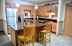 A kitchen with a refrigerator, two chairs, and a countertop.