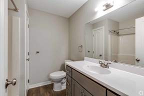A white toilet sits in a small bathroom with a sink and mirror.