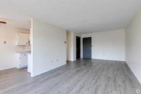 A spacious room with a kitchenette and a door leading to another room.