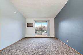 A room with a grey carpet and a window overlooking a balcony.