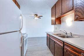 A kitchen with a white fridge, wooden cabinets, and a ceiling fan.