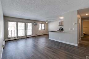 A spacious living room with hardwood floors and a kitchenette in the background.