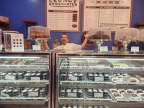 a man standing behind the counter of a display case of donuts