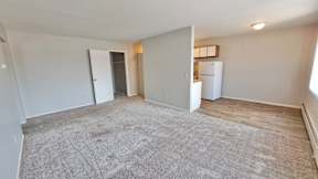 A spacious living room with a grey carpet and white walls.