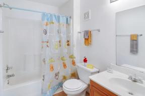 A white toilet with a blue shower curtain with orange and green designs on it.