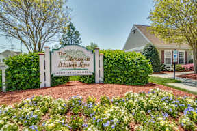 A sign for The Glens at Thillers Lane Apartment Homes is surrounded by flowers.