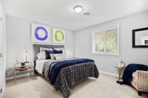 A bedroom with a bed, a chair, and a mirror.