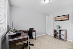 A room with a desk, chair, and a shelf.