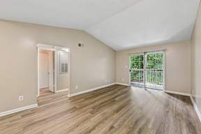 A room with wooden flooring and a sliding glass door leading to a balcony.
