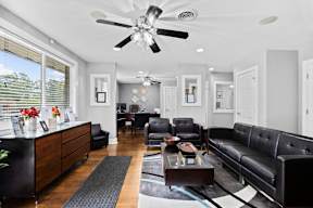 A black leather couch sits in a well-lit living room with a ceiling fan overhead.