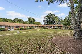 A grassy area in front of a building with a tree on the right.