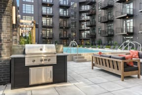 an outdoor kitchen with a grill next to a pool and an apartment building in the background at Crossline, Columbus