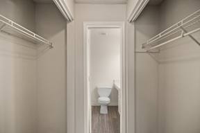 A white toilet is in a small bathroom with white walls and wood flooring.