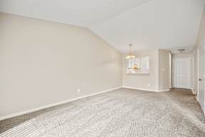 A large, empty room with a carpeted floor and a chandelier hanging from the ceiling.