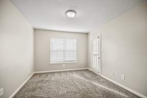 A room with a carpeted floor and a window with blinds.