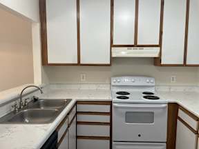 A white stove is in a kitchen with white cabinets.
