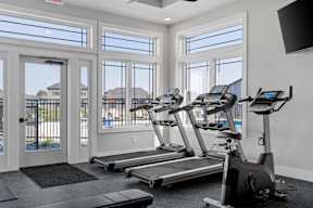 A gym with treadmills and a television mounted on the wall.
