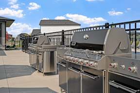 A row of stainless steel outdoor grills are lined up on a patio.