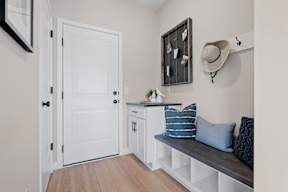 A white door is open to a hallway with a bench and a hat hanging on the wall.