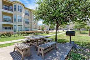 A wooden picnic table is surrounded by benches in a concrete courtyard.