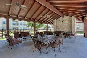 A patio with a table and chairs under a wooden roof.
