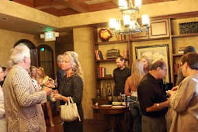 A group of people are standing in a room with a chandelier and bookshelves.