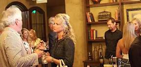 A man is handing a glass to a woman in a room with a bookshelf.