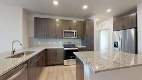 A modern kitchen with a granite countertop and stainless steel appliances at Railside at Wadsworth Station, Lakewood, 80214