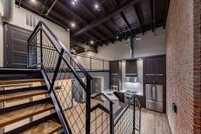 A staircase with a metal railing leads to a kitchen area.
